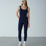 Person wearing a navy blue sleeveless jumpsuit with white sneakers on a plain background