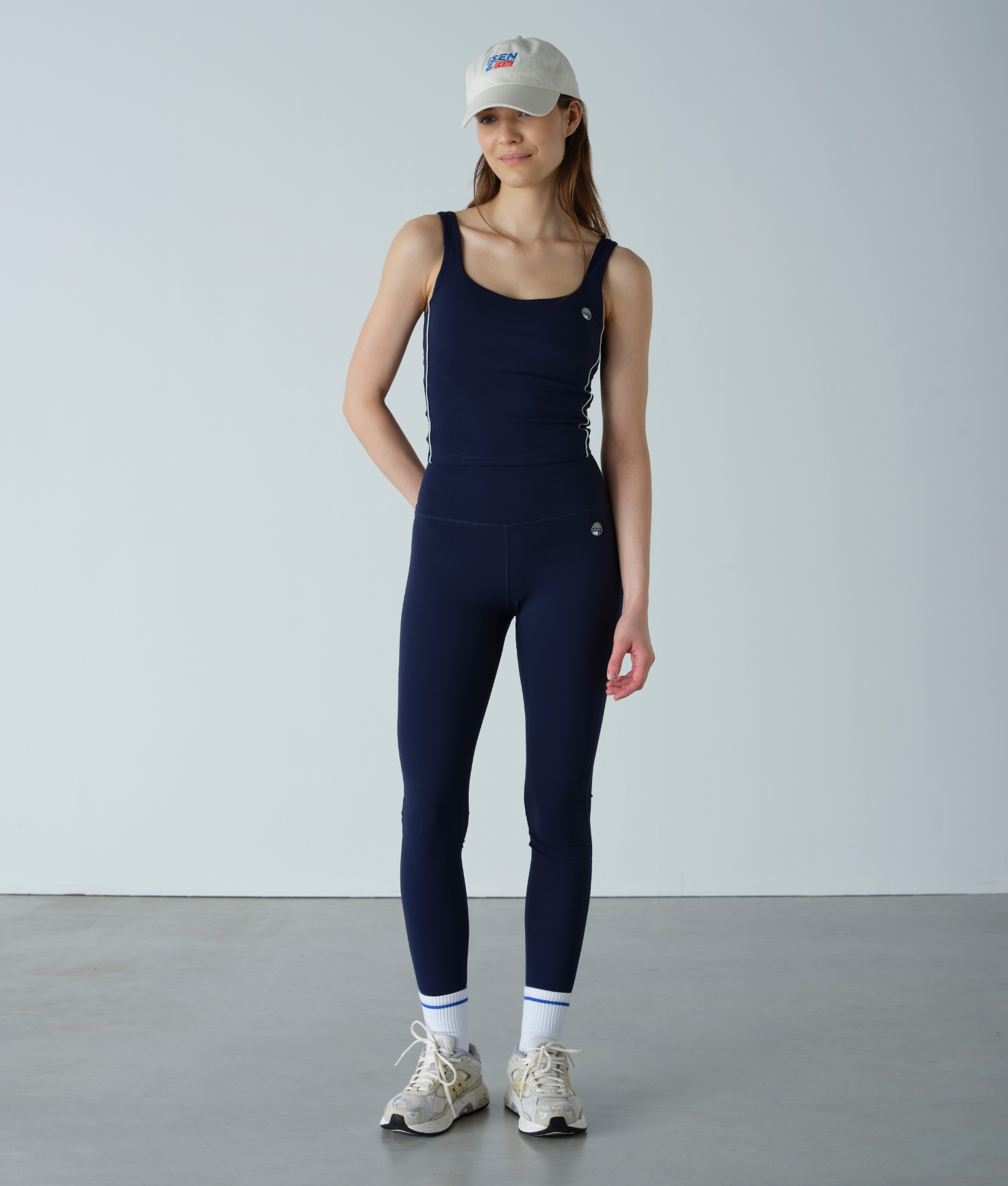 Person wearing a navy blue sleeveless jumpsuit with white sneakers on a plain background