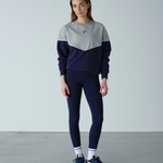 Person wearing a gray and navy color-blocked sweater with navy leggings on a plain background