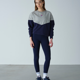 Person wearing a gray and navy color-blocked sweater with navy leggings on a plain background