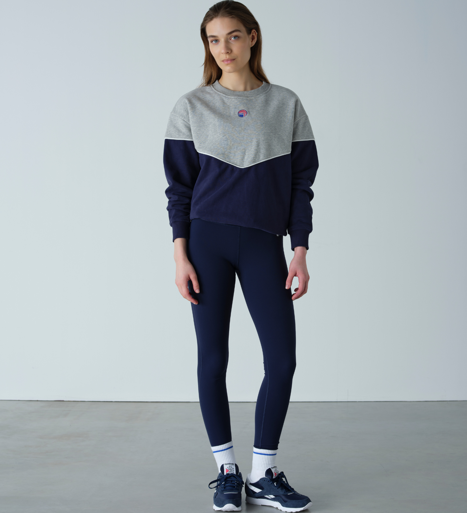 Person wearing a gray and navy color-blocked sweater with navy leggings on a plain background