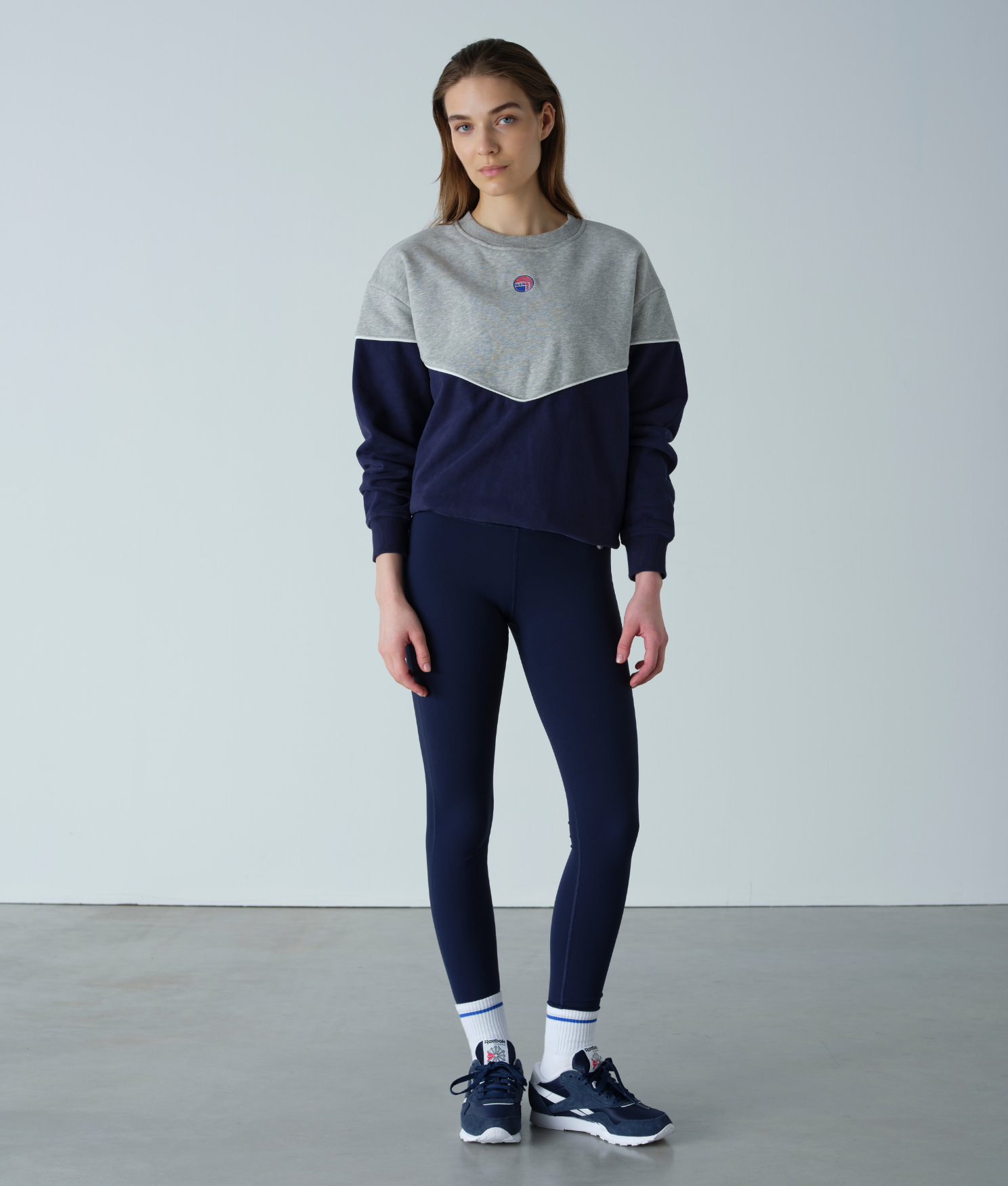 Person wearing a gray and navy color-blocked sweater with navy leggings on a plain background