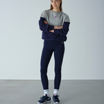 Woman wearing a gray and navy tracksuit with a logo on a plain background