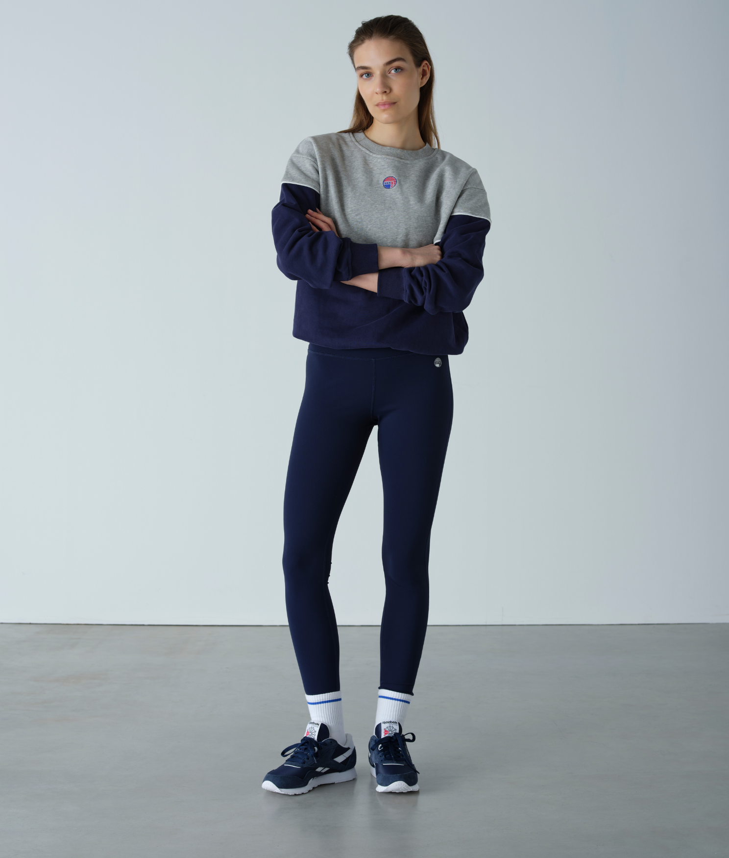 Woman wearing a gray and navy tracksuit with a logo on a plain background