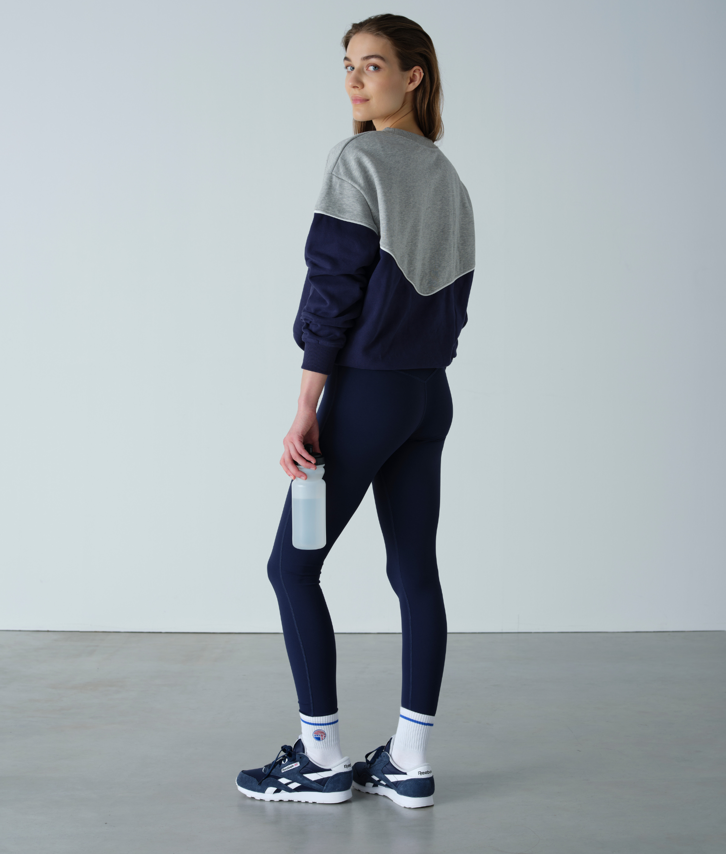 Person wearing a two-tone sweatshirt and leggings set, holding a water bottle against a plain background.