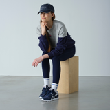 Person wearing a navy and gray outfit sitting on a wooden block against a plain background