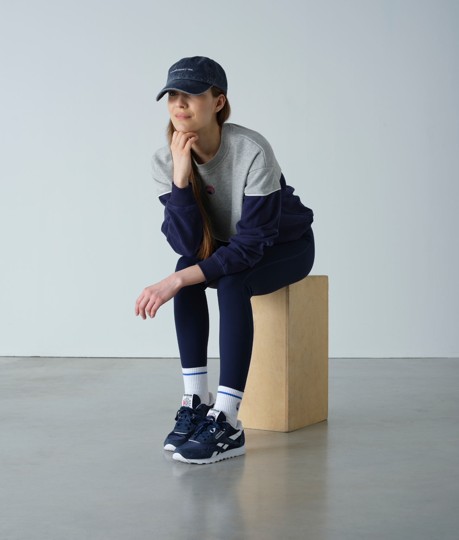 Person wearing a navy and gray outfit sitting on a wooden block against a plain background