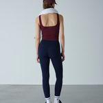 Person wearing a maroon tank top and navy leggings with a white towel over their shoulder against a plain background.