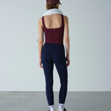 Person wearing a maroon tank top and navy leggings with a white towel over their shoulder against a plain background.