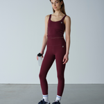 Woman wearing a maroon athletic outfit with leggings and a tank top, standing against a plain background.