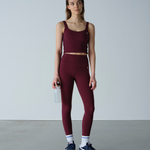 Woman wearing a maroon athletic outfit holding a water bottle on a plain background
