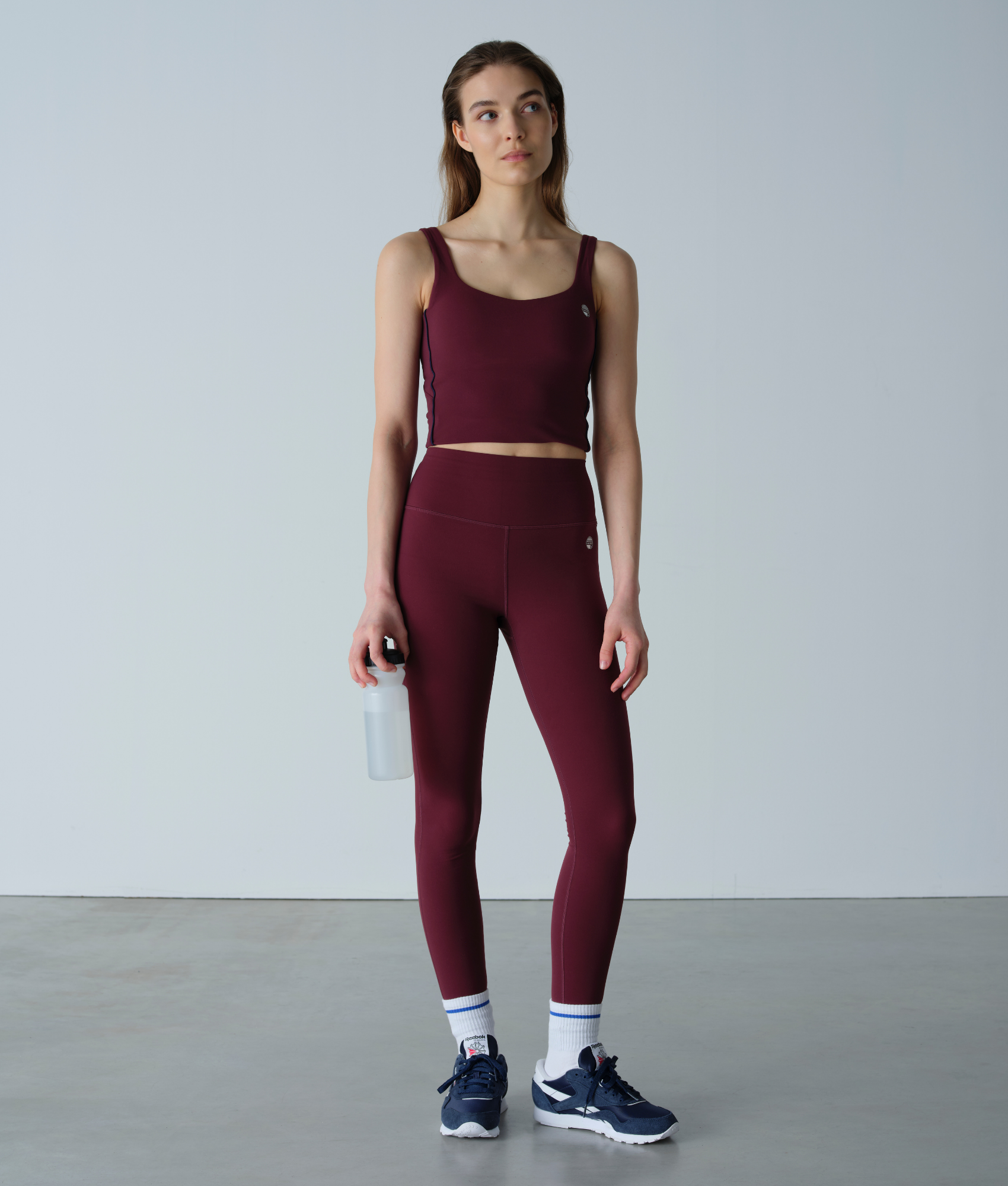 Woman wearing a maroon athletic outfit holding a water bottle on a plain background