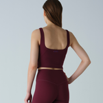 Woman wearing a maroon sports bra and leggings on a light gray background