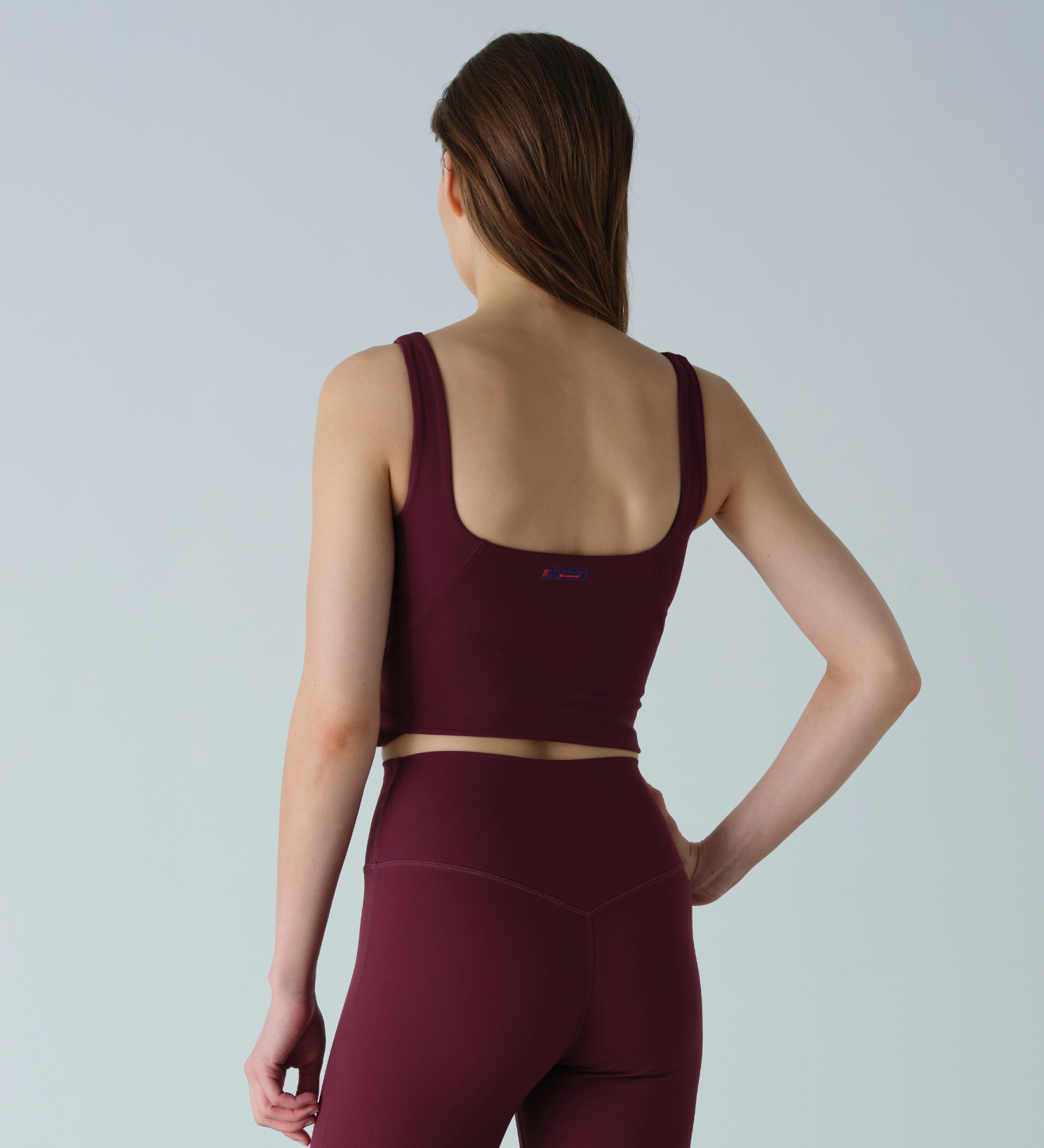 Woman wearing a maroon sports bra and leggings on a light gray background