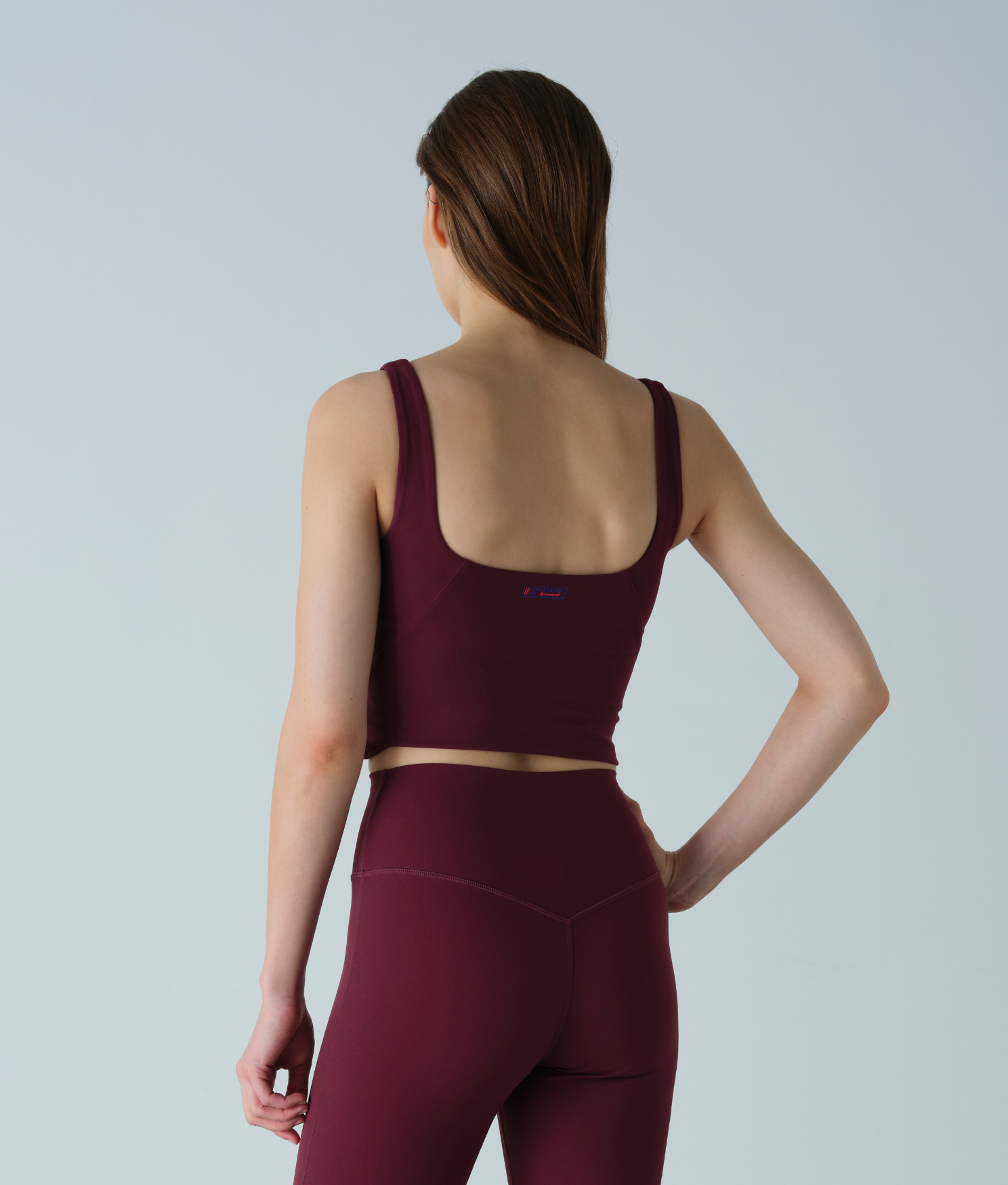 Woman wearing a maroon sports bra and leggings on a light gray background