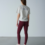 Person wearing a light gray t-shirt and maroon leggings against a plain background