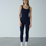 Woman wearing a navy blue sleeveless top and leggings set against a plain background