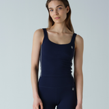 Woman wearing a navy blue tank top and leggings on a light gray background