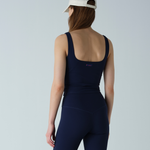 Person wearing a navy tank top and leggings with a white cap on a light gray background